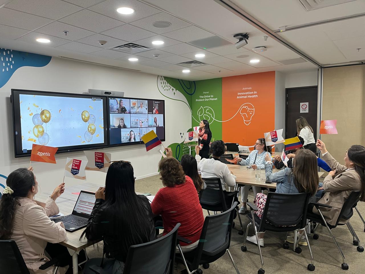 Alejandra leading a team meeting, colleagues around the table and others joining on screen