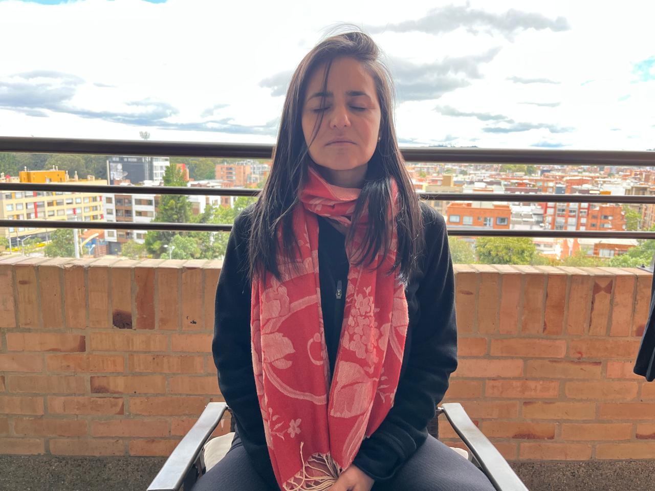 Alejandra meditating with her eyes closed on a balcony above the city